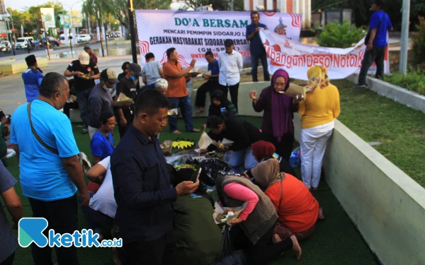 Foto Para aktivis antikorupsi GM-SBAK bersama warga menikmati tumpeng selamatan di Alun-Alun Sidoarjo pada Selasa (30/7/2023). (Foto: Fathur Roziq/Ketik.co.id)