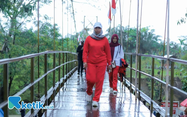 Foto Pj Bupati Nagan Raya, Fitriany Farhas berjalan di jembatan gantung Irigasi Beutong untuk mengikuti apel pembentangan bendera berukuran raksasa, Minggu (18/8/2024). (Foto: Dekwan/Ketik.co.id)