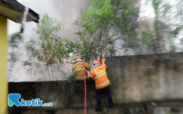 Foto Dua orang petugas pemadam kebakaran memanjat dinding pembatas untuk memadamkan api yang membakar tempat usaha rongsokan di Jalan R Kemuning, RT 23 Kelurahan Ario Kemuning, Kecamatan Kemuning, Kota Palembang, Jumat 15 November 2024. (Foto: Wisnu Akbar Prabowo/Ketik.co.id)