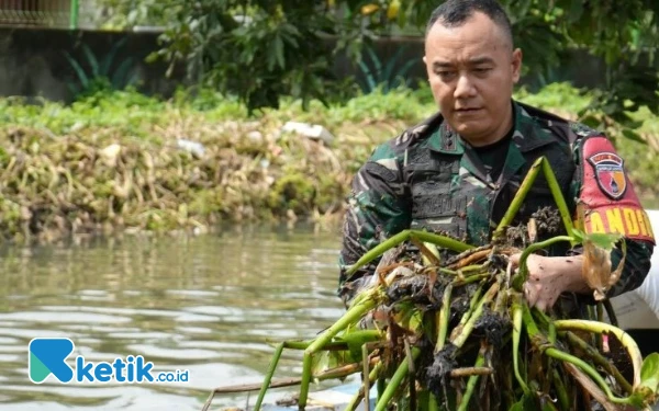 Foto Dandim Sidoarjo Letkol Inf Dedyk Wahyu Widodo membersihkan enceng gondok yang menyumbat aliran sungai di Kecamatan Waru pada Kamis (26 Desember 2024). (Foto: Dinas Kominfo Sidoarjo)