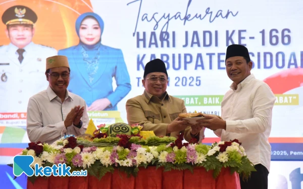 Foto Plt  Bupati Sidoarjo Subandi (kanan) menerima potongan tumpeng dari KH Ahmad Aziz didampingi Ketua DPRD Sidoarjo Abdillah Nasih. (Foto: Sigit Kominfo Sidoarjo).