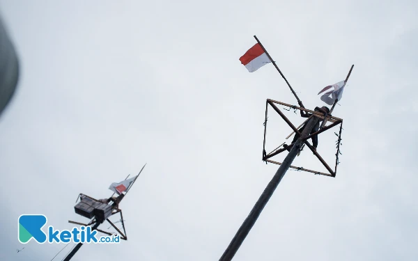 Thumbnail Seorang anak mengibarkan bendera merah putih usai menurunkan seluruh hadiah yang digantung di batang pinang, Minggu (18/8/24). (Foto: Wisnu Akbar Prabowo/Ketik.co.id)