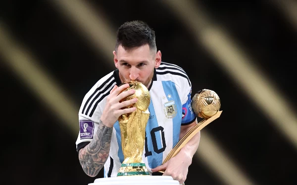 Foto Lionel Messi mencium trofi Piala Dunia di podium juara. (Foto: FIFA+)