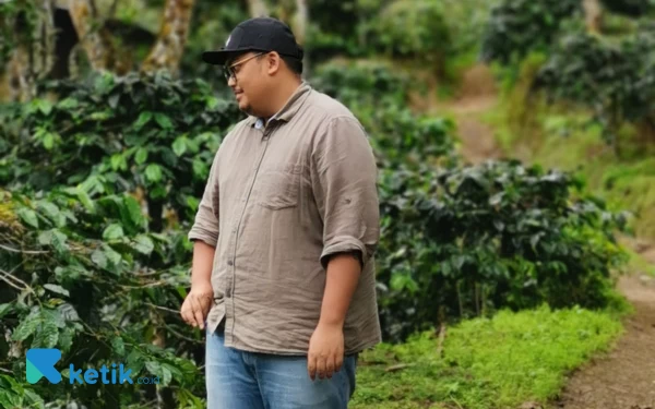 Foto Dhani berfoto dengan latar belakang pohon kopi.