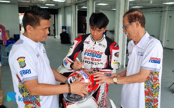 Foto Mario Aji menandatangani helm batik persembahan untuk Bupati Magetan Suprawoto (kacamata), didampingi Manager Kiagus Firdaus di Sirkuit Mandalika. (Foto: Ias Abdullah/Ketik.co.id)