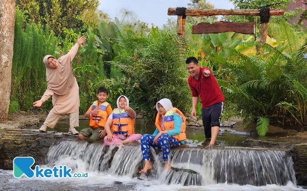 Foto Seperti lukisan hidup, pengunjung keluarga yang sedang berfoto di area mini air terjun Cemerlang Asri.