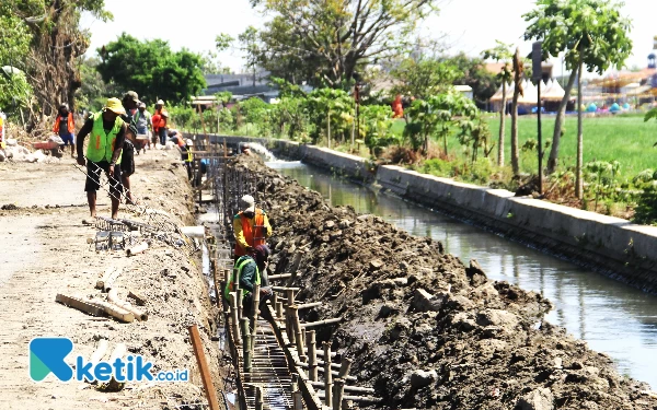 Foto Pekerja menggarap konstruksi besi jalan beton ruas Damarsih—Banjarsari, Buduran, yang berdekatan dengan saluran air. (Foto: Fathur Roziq/Ketik.co.id)