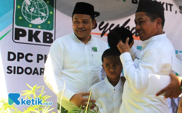 Foto Ketua DPC PKB Sidoarjo H Subandi SH (kiri) dan legislator PKB H Mohammad Rojik menolong seorang anak yatim yang terlihat sakit saat menerima santunan dalam perayaan Harlah Ke-25 PKB pada Sabtu (28/7/2023). (Foto: Fathur Roziq/Ketik.co.id)