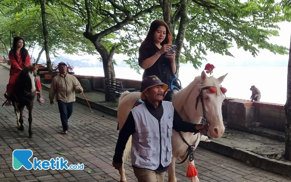 Foto Wisatawan mengelilingi Telaga Sarangan dengan menaiki kuda.