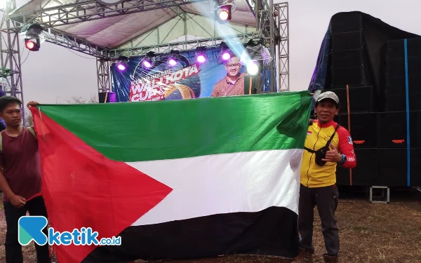 Foto Ridwan Asnan (kanan) berfoto dengan bendera Palestina usai terbang dengan Paralayang. (Foto: Sholeh/ketik.co.id)