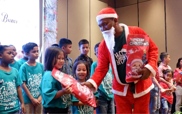 Foto Maskot natal Santa Claus saat membagikan hadiah natal kepada anak-anak panti asuhan. (Foto: Dok Premier Place Hotel Surabaya Airport)