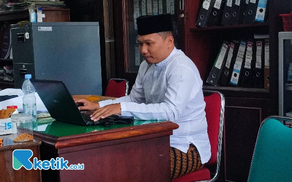 Foto ASN Zaenal Arifin tengah bekerja dengan mengenakan pakaian khas santri, berbaju koko, berkopiah lengkap mengenakan sarung.  (Foto: Al Ahmadi/Ketik.co.id)